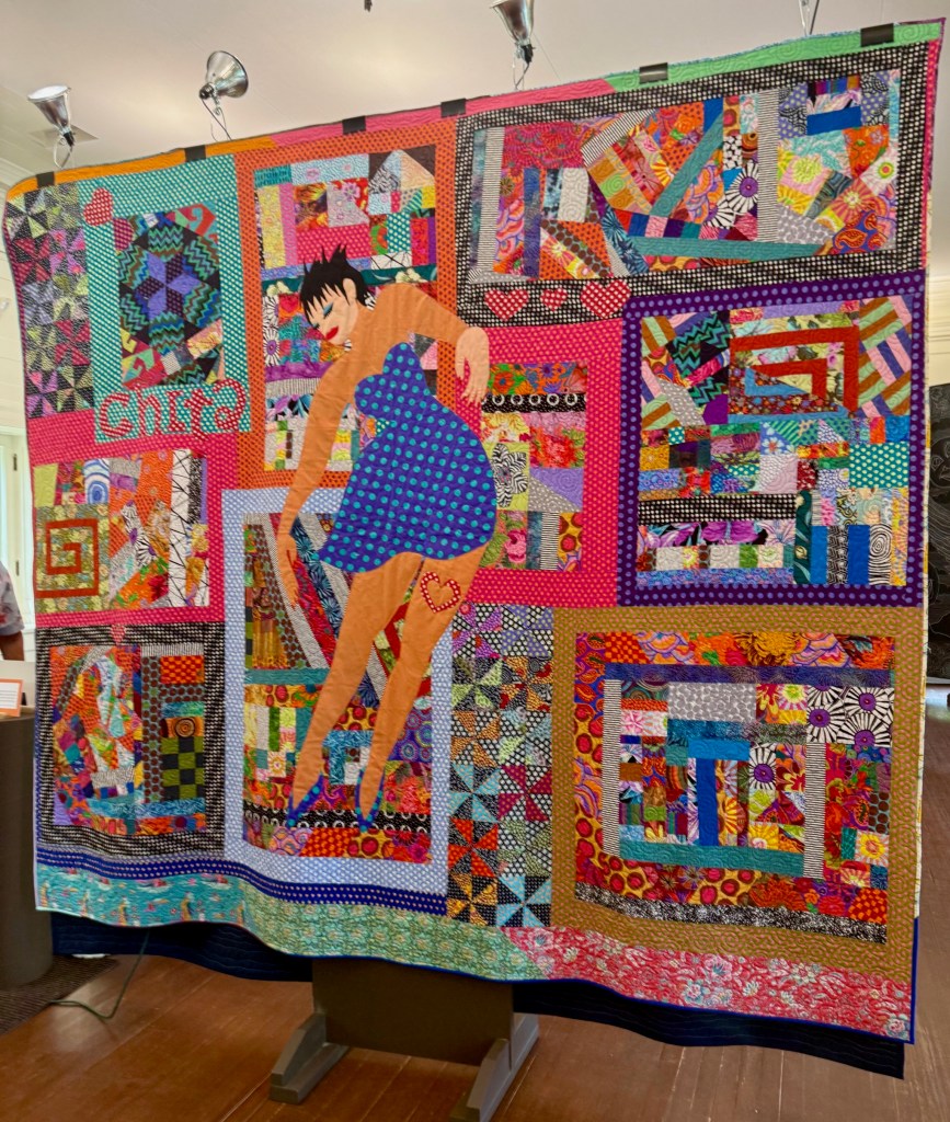 A colorful quilt titled 'Chita', featuring an abstract female figure surrounded by vibrant patchwork patterns.
